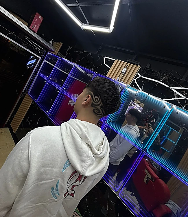 Diseño de líneas curvas tallado en la nuca, frente a una vitrina de cubos con luz azul neón y el techo de hexágonos