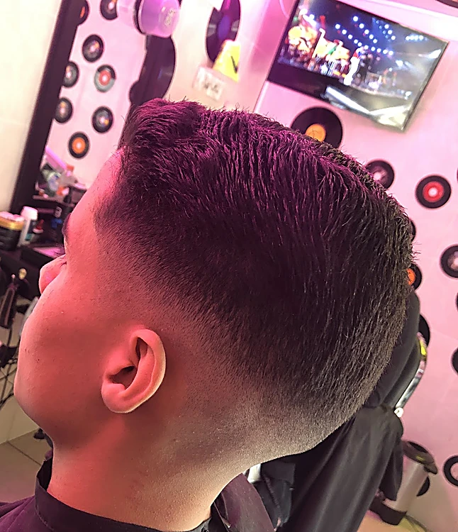 Fade con cabello texturizado arriba, visto de espaldas frente a una pared de discos de vinil